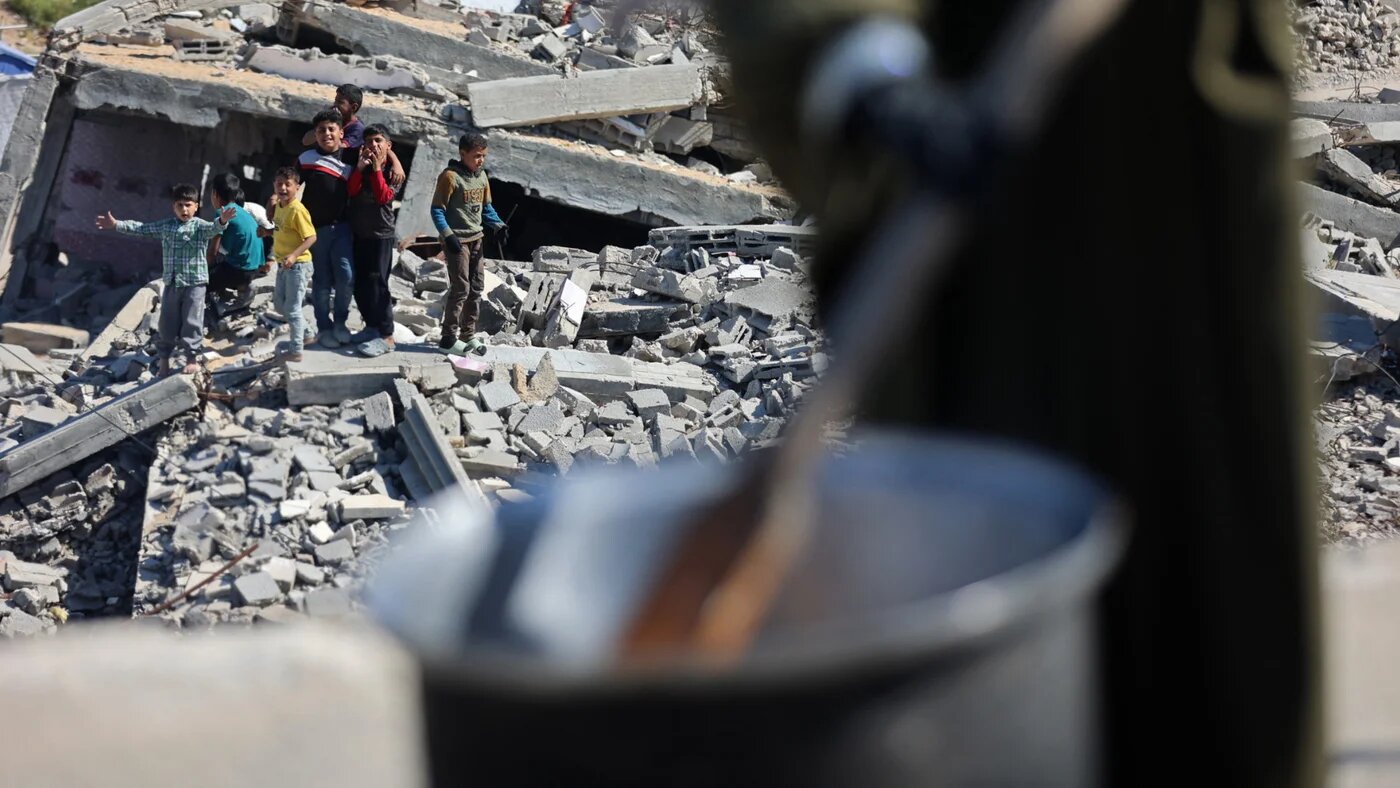 Displaced children stand on the rubble of destroyed houses as they watch the food being prepared by a charity in the northern Gaza Strip on 6 May 2026 (Omar al-Qattaa/AFP)