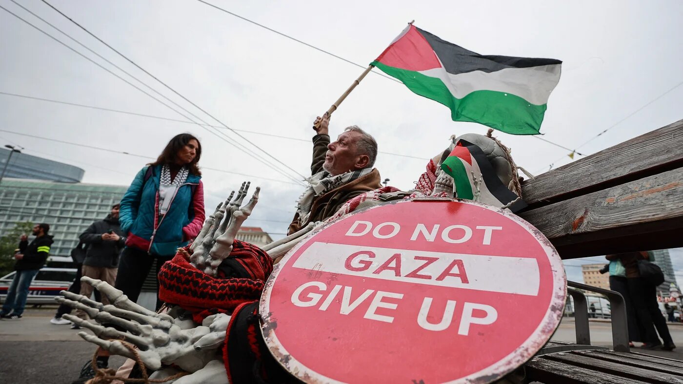 A man holds a Palestinian flag beside a sign reading "Do not give up Gaza" during a protest in Vienna on 12 May 2026 (Radek Mica/AFP)