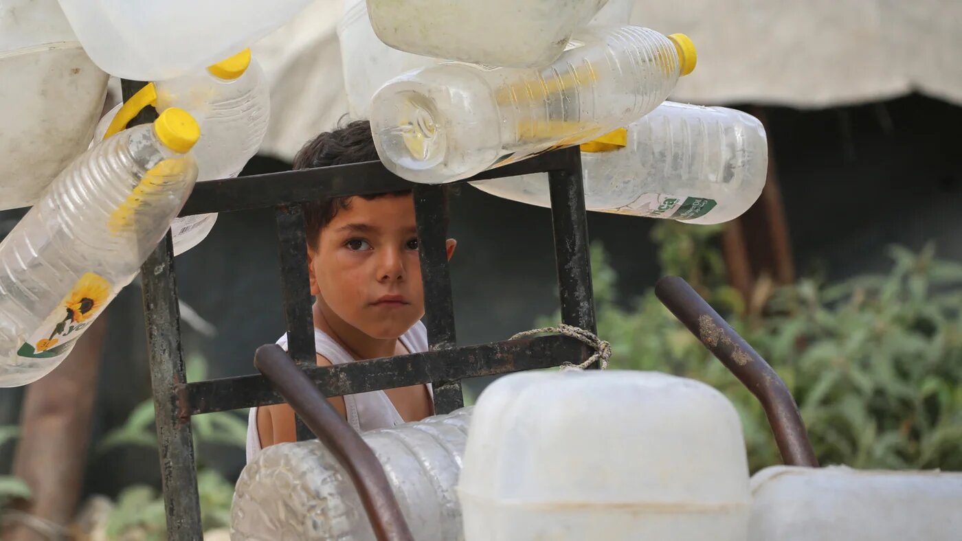 A Palestinian boy stands next to plastic containers on a trolley, as he and others collect portable water for their displaced family living in shelters in the Bureij refugee camp, in the central Gaza Strip on 18 May 2026 (Eyad Baba/AFP)