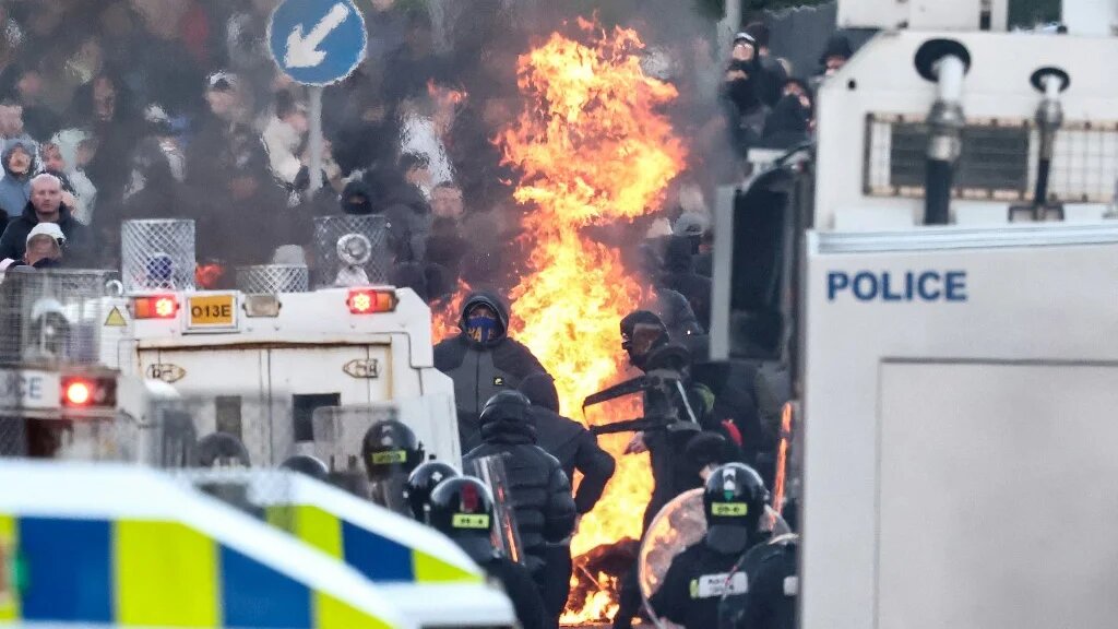 Protesters (behind) stand off with police as the former block a road leading to a hotel previously believed to house migrants, in Glengormley, north of Belfast, Northern Ireland, on June 10, 2026. 
