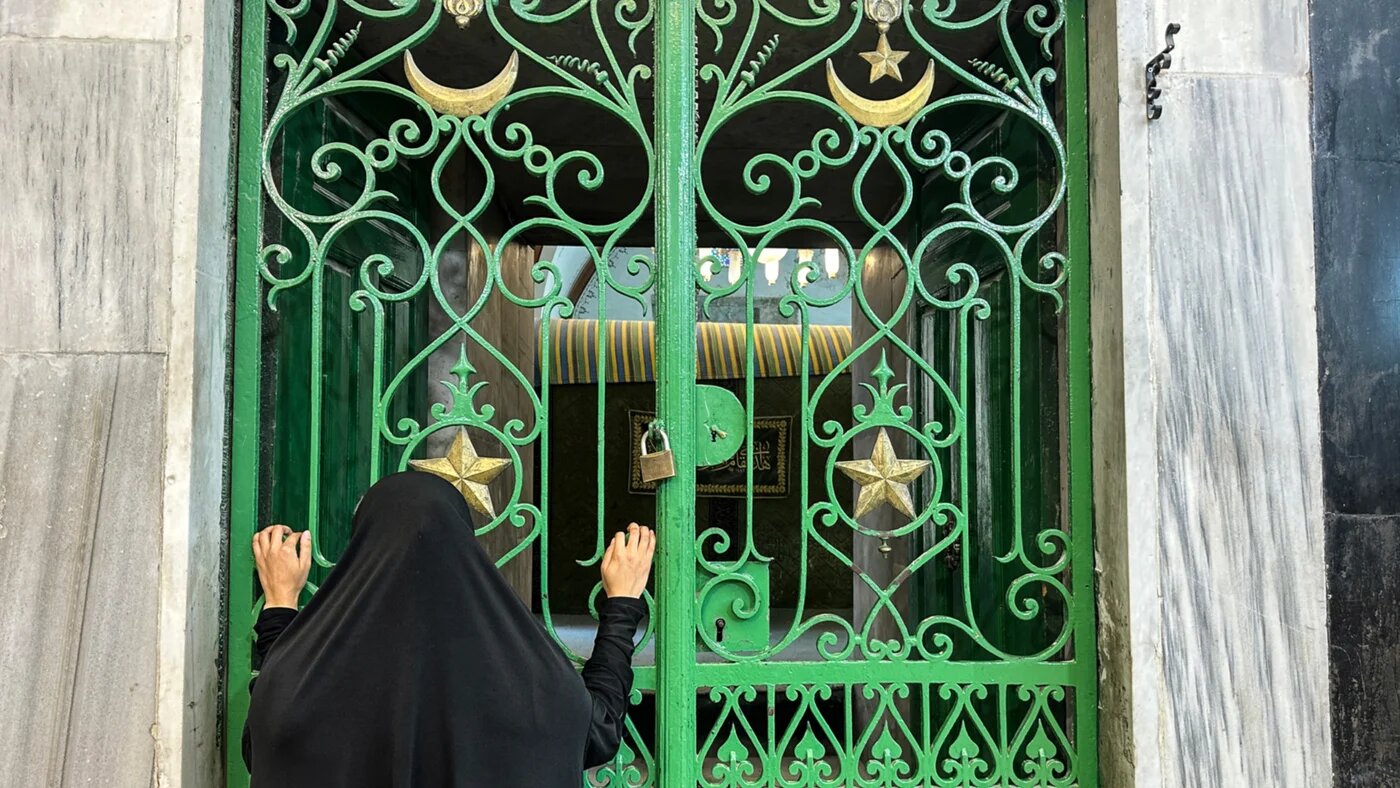 A woman looks through an iron gate at the Ibrahimi Mosque in the occupied West Bank city of Hebron, on 16 June 2026 (Hazem Bader/AFP)