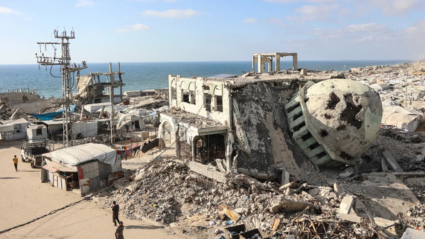 Displaced Palestinians walk past destroyed buildings and makeshift shelters near the al-Shati refugee camp, west of Gaza City, on 1 July 2026 (Omar  al-Qattaa/AFP)