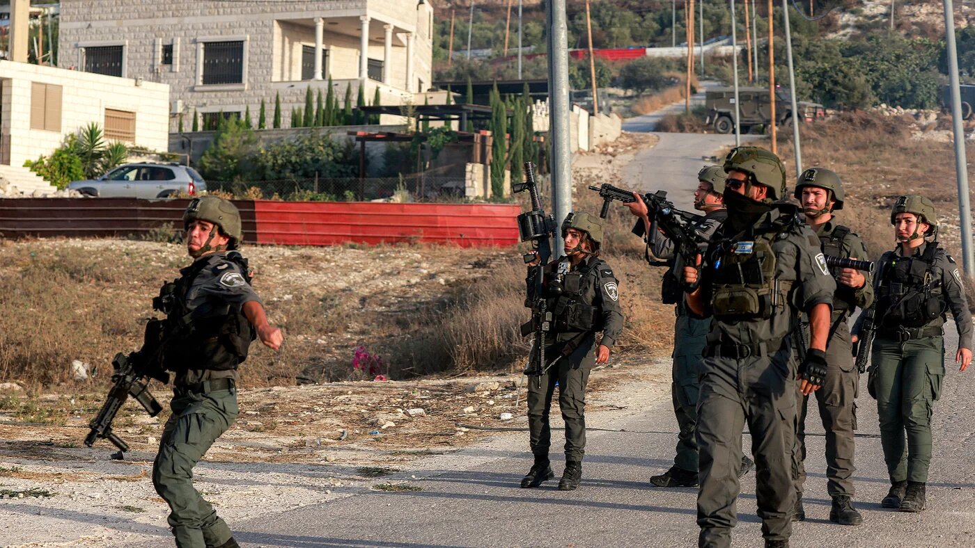Armed Israeli soldiers in combat gear walk through a street in the Palestinian village of Tell in the occupied West Bank