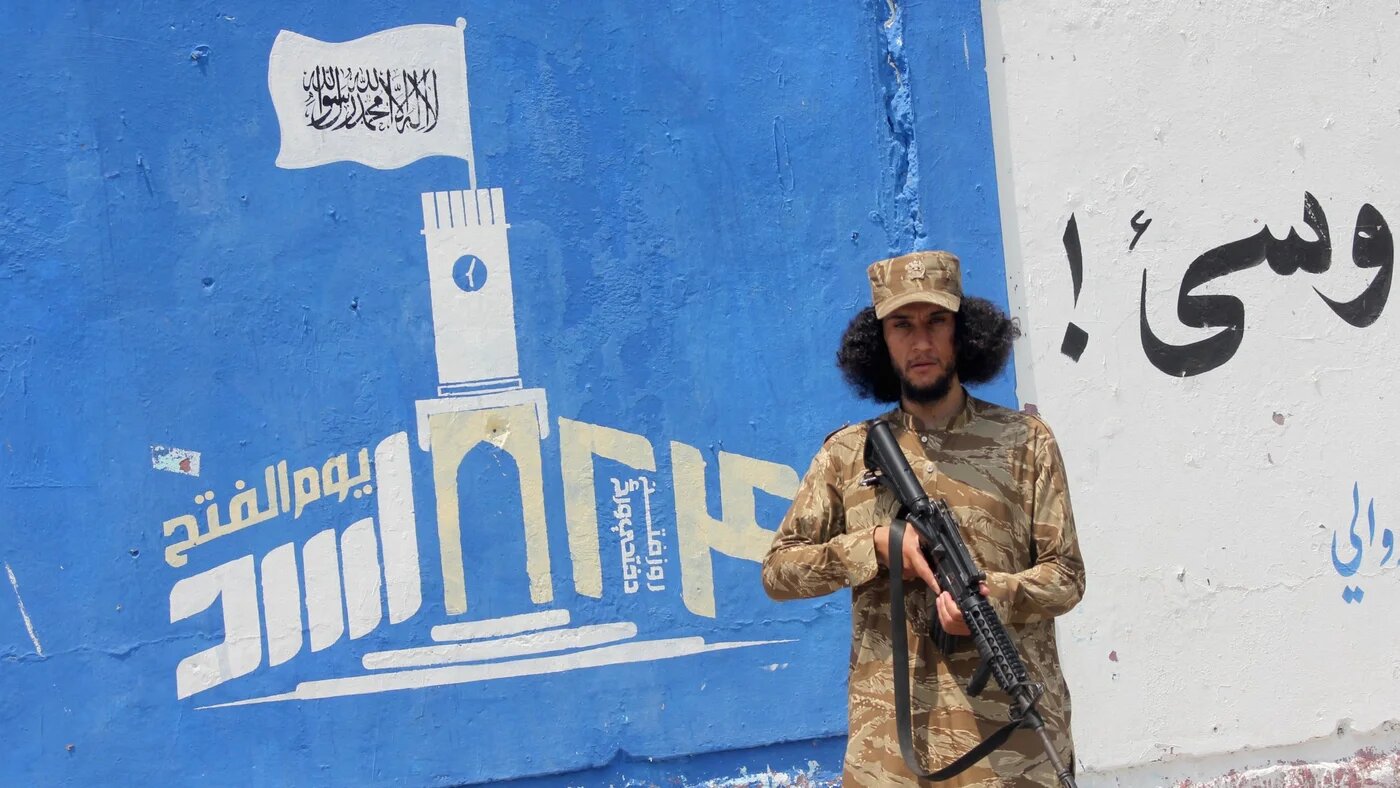 A security personnel stands guard next to a mural depicting the Taliban flag, along a street in Jalalabad, Afghanistan, ahead of the fifth anniversary of the Taliban's takeover of the country, on 12 August 2026 (Aimal Zahir/AFP)