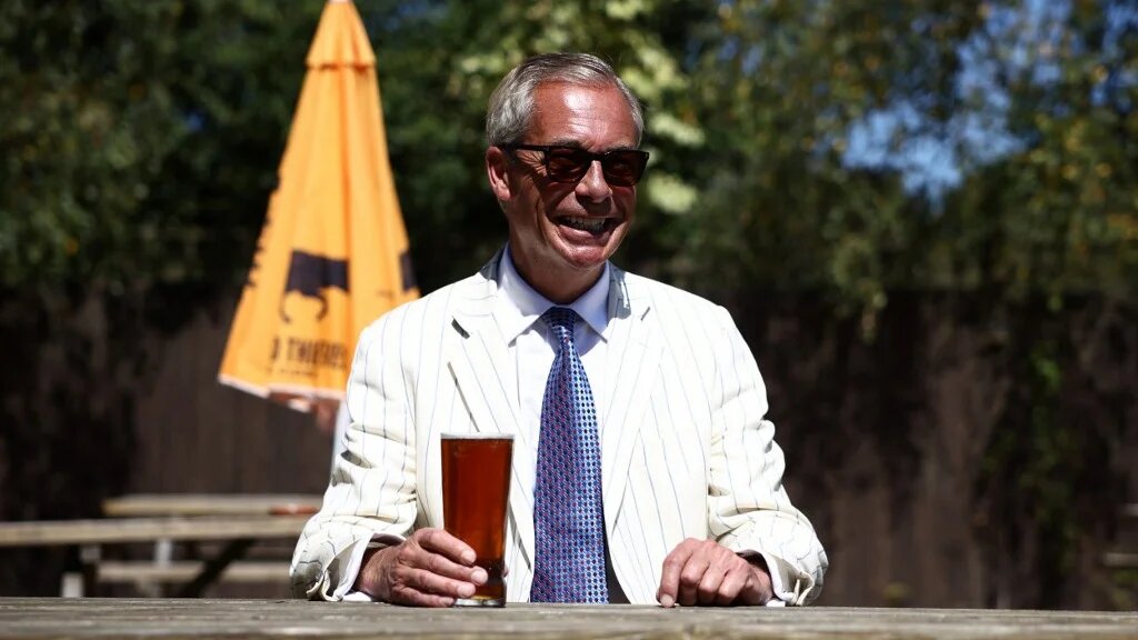 Reform UK leader Nigel Farage poses with a pint at The Ship pub after casting his vote in the Clacton by-election, in the village of Kirby-le-Soken, Essex on 13 August 2026 (AFP)