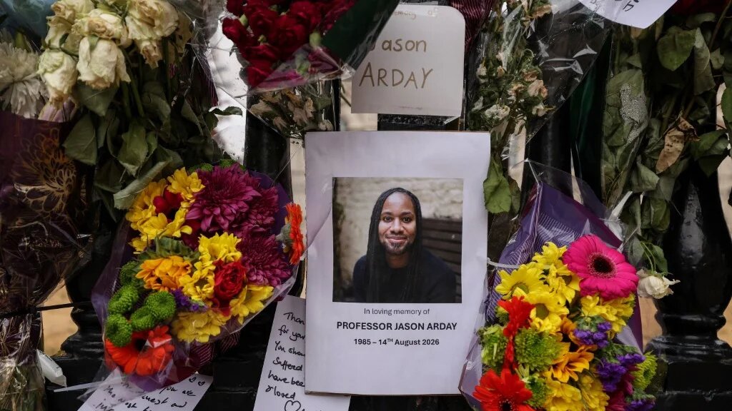 A photo (C) of late Cambridge professor Jason Arday is pictured along with floral tributes, attached to the fencing around the Senate House at the University of Cambridge on August 18, 2026. (AFP)