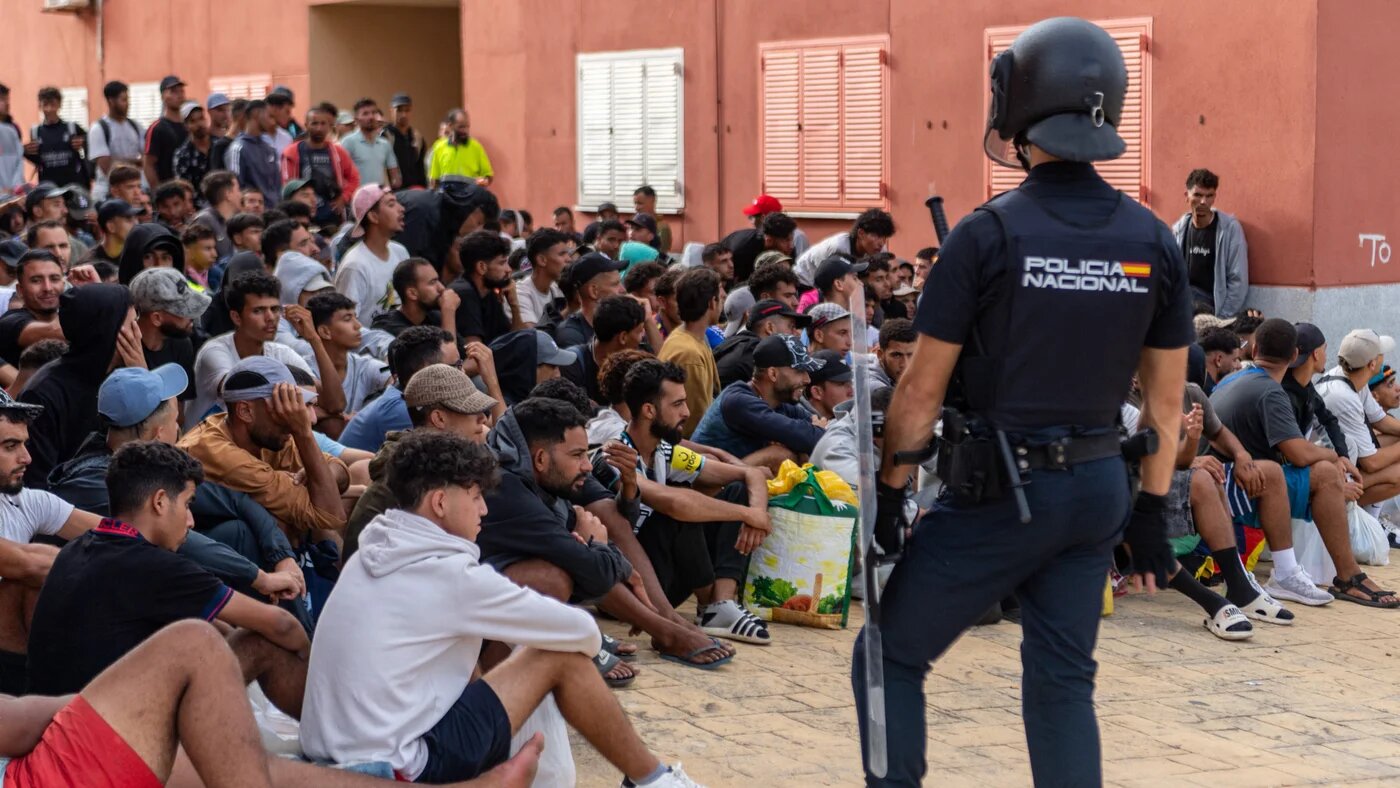 A Spanish police officer stands guard as migrants wait to be registered in the Loma Colmenar district of Ceuta on 31 August 2026 (Antonio Sempere/AFP)