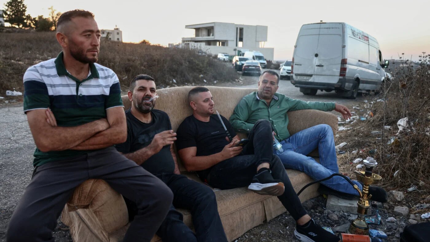 People sit on a sofa with a waterpipe to watch as commuters wait in their vehicles at the Israeli Atara checkpoint on Route 465 near Ramallah in the occupied West Bank on 27 September 2026 (Zain Jaafar/AFP)