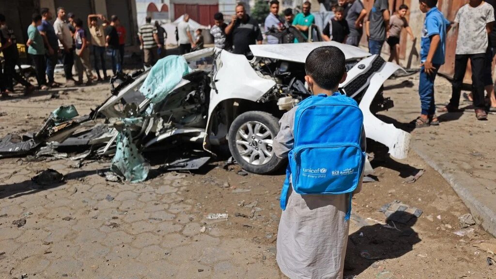 A Palestinian boy carrying UNICEF bag, looks at the wreckage of a car after it was destroyed in Israeli strike at the Tuffah neighborhood of Gaza City on October 13, 2026. (Omar Al-Qattaa/AFP)