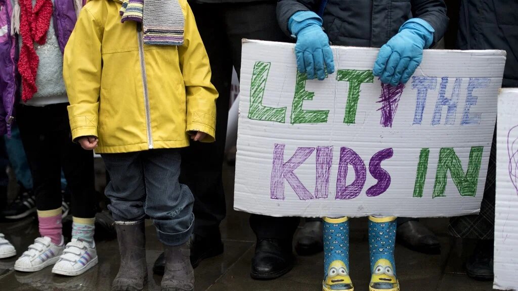 A child holds a placard that reads "Let the kids in" during a protest for refugees in London on February 11, 2017 (AFP) 
