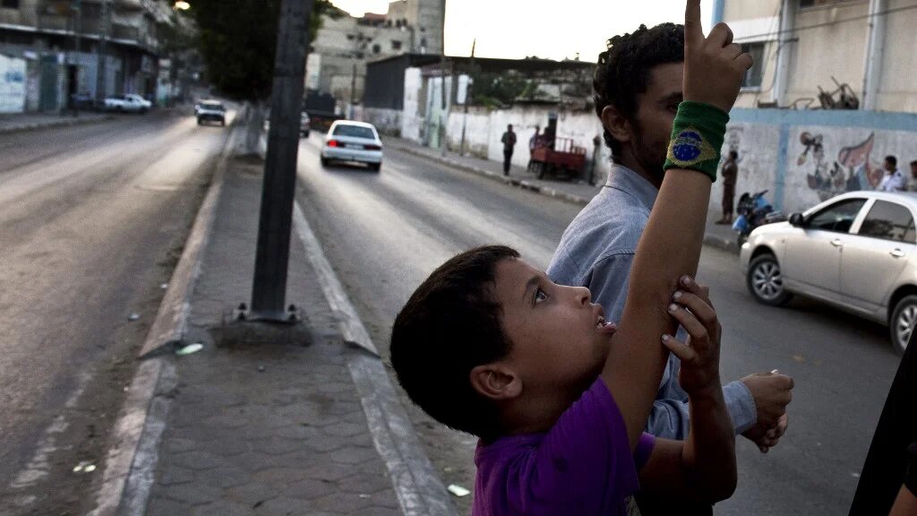 Un garçon palestinien pointe son doigt vers le ciel afin de montrer deux drones israéliens survolant l’enclave palestinienne de Gaza (AFP/Roberto Schmidt) 