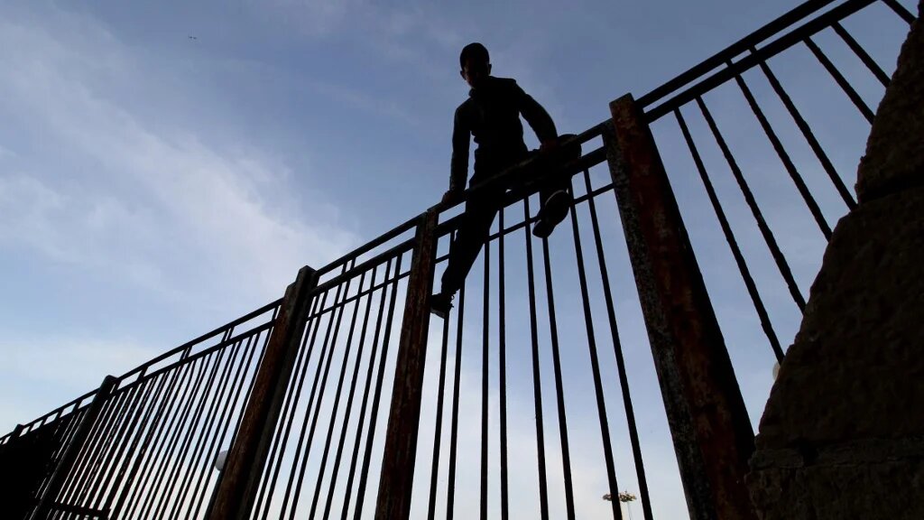 Un jeune garçon escalade une des clôtures de l’enclave espagnole de Melilla à la frontière du Maroc, le 16 mai 2017 (AFP/Antonio RUIZ)
