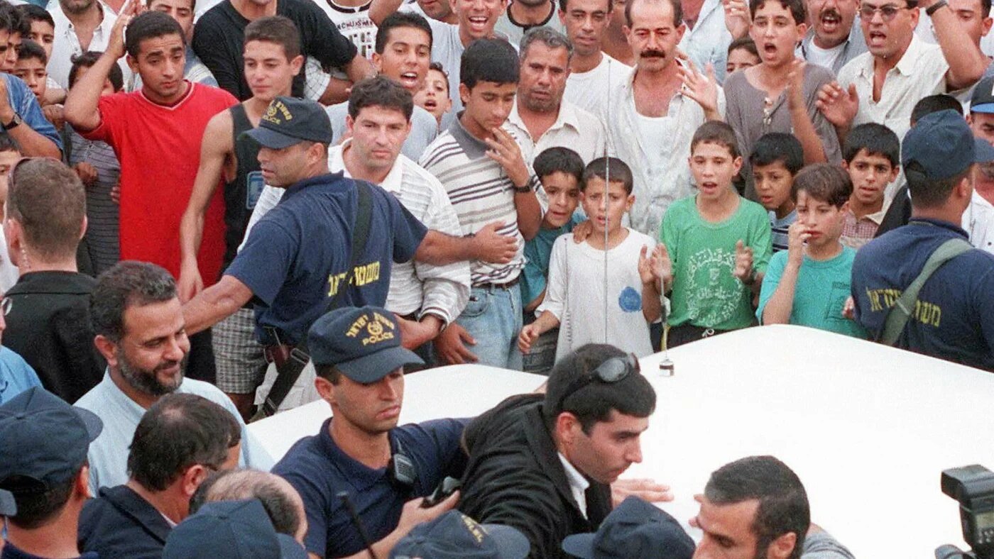 Des citoyens palestiniens d’Israël brandissent des pancartes sur lesquelles on peut lire en hébreu ce qui signifie « Pardon des bouchers », alors que le vice-Premier ministre israélien Moshe Katsav quitte Kafr Qasim, le 29 octobre 1997 (AFP)