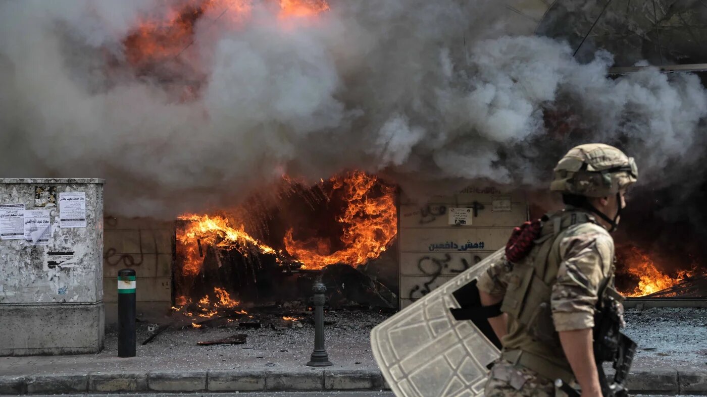 A soldier walks past a burning bank branch in Tripoli, Lebanon on 28 April 2020, during protests following the death of Fawaz Fouad Samman, a 26-year-old demonstrator shot by the army the previous night (MEE/Elizabeth Fitt)
