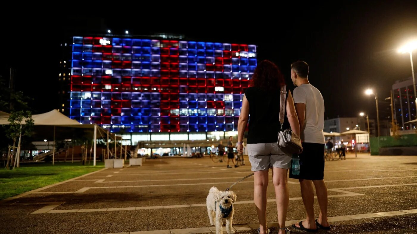 Des promeneurs s’arrêtent avec leur chien sur la place Rabin de Tel-Aviv, face à la mairie illuminée aux couleurs du drapeau britannique en hommage à la reine Elizabeth II (Reuters)