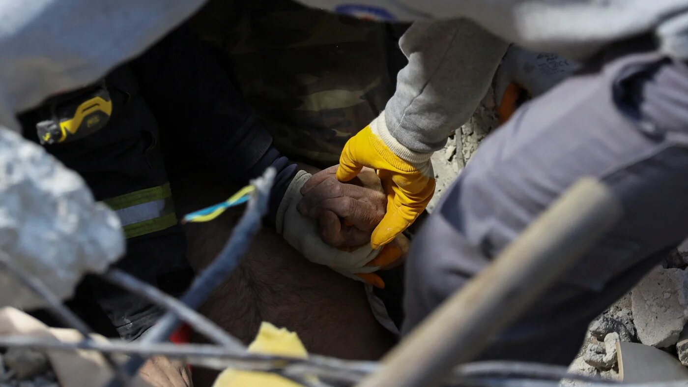 Rescuers work hold the hand of a survivor as search efforts enter critical point in the aftermath of a deadly earthquake in Hatay, Turkey 9 February 2023 (Rueters)