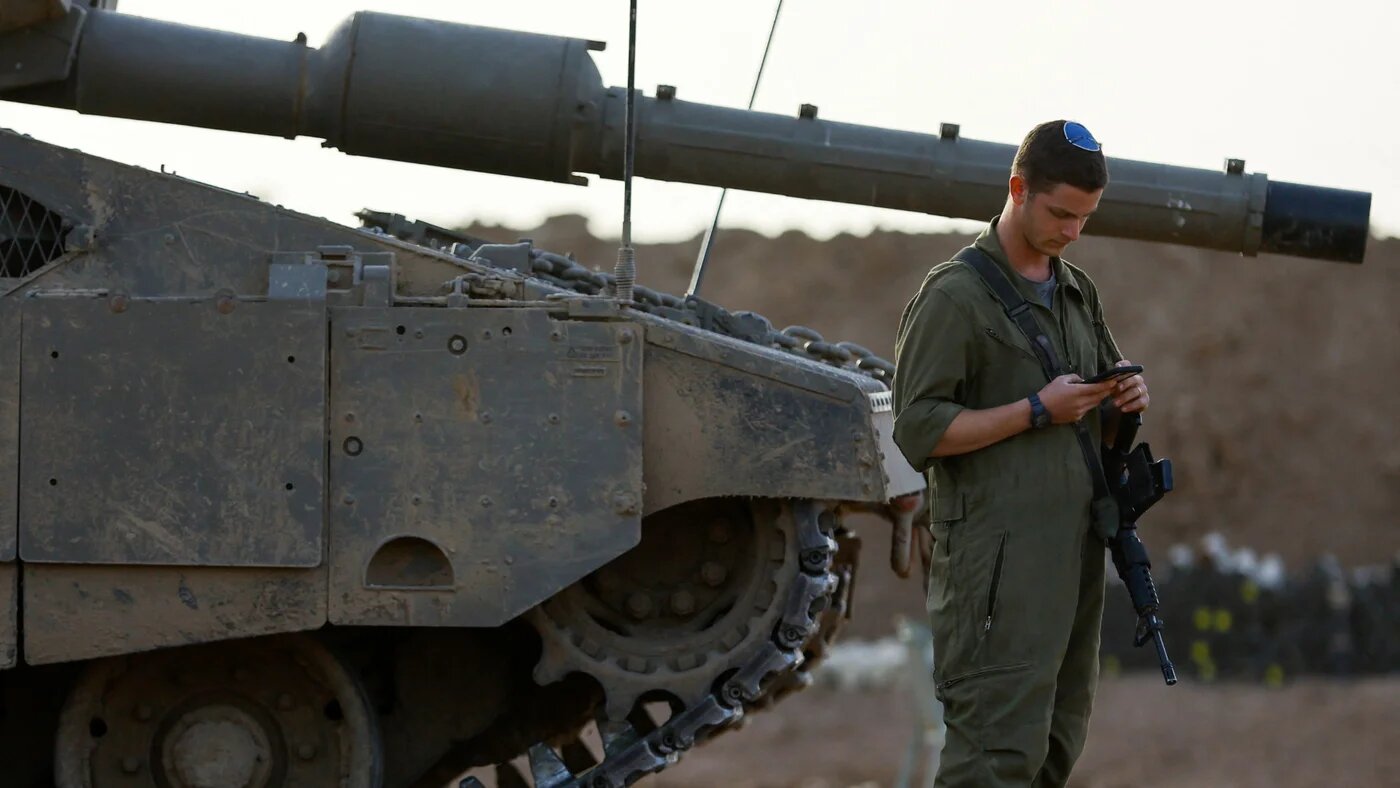 An Israeli soldier uses a mobile phone near the boundary with Gaza on 26 November 2023 (Reuters/Alexander Ermochenko)