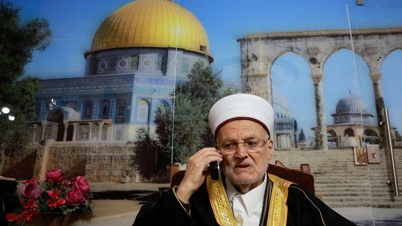 Sheikh Ekrima Sabri, the preacher of Jerusalem's Al-Aqsa mosque, speaks on the phone in his living room after an interview with Reuters in Jerusalem, 21 February 2024 (Reuters/Ammar Awad)