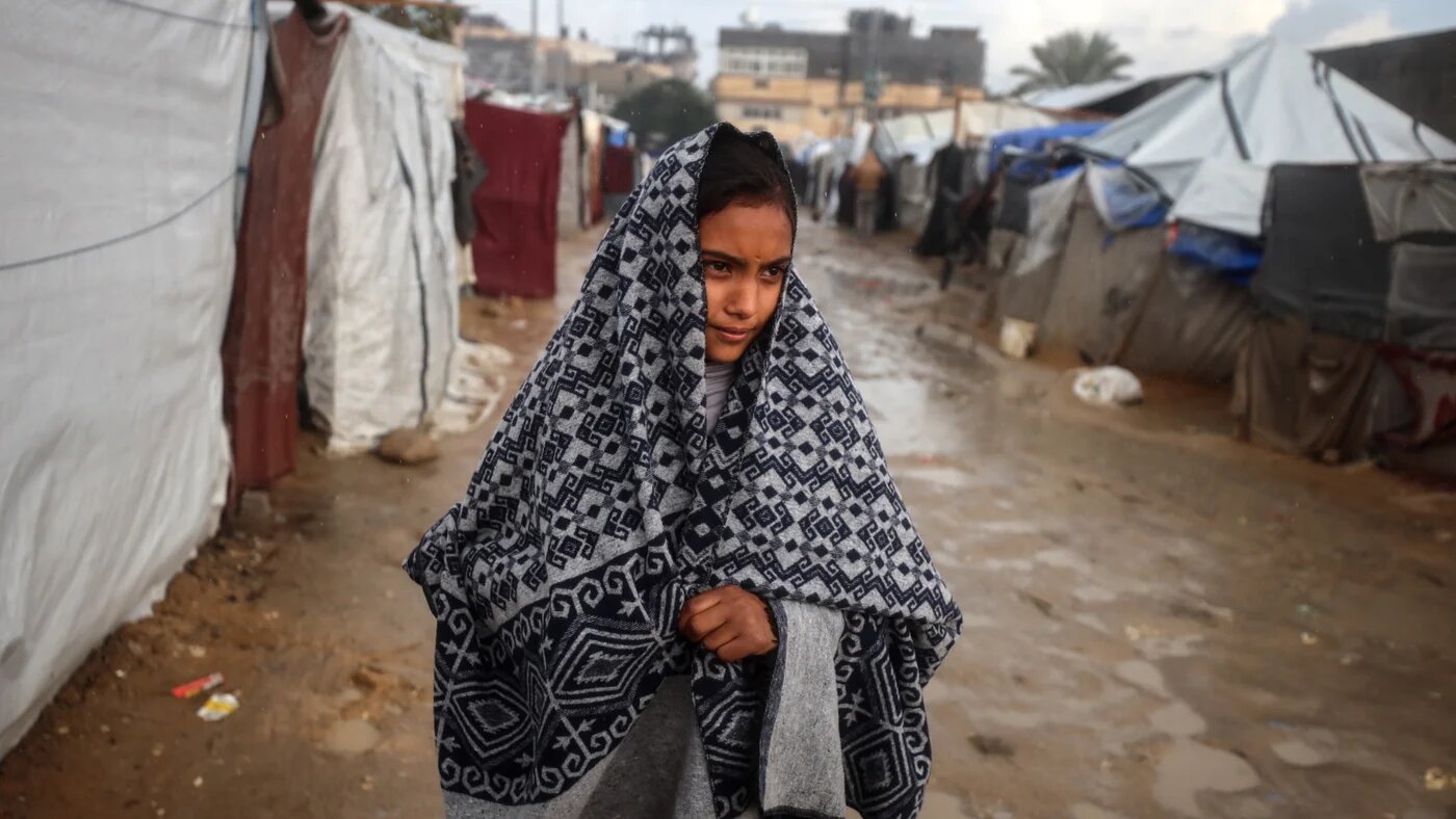 A displaced Palestinian girl looks at a tent camp following heavy rains amid the Israeli war on Gaza in Deir al-Balah, in the central Gaza Strip, on 31 December 2024 (Majdi Fathi/NurPhoto via Reuters)