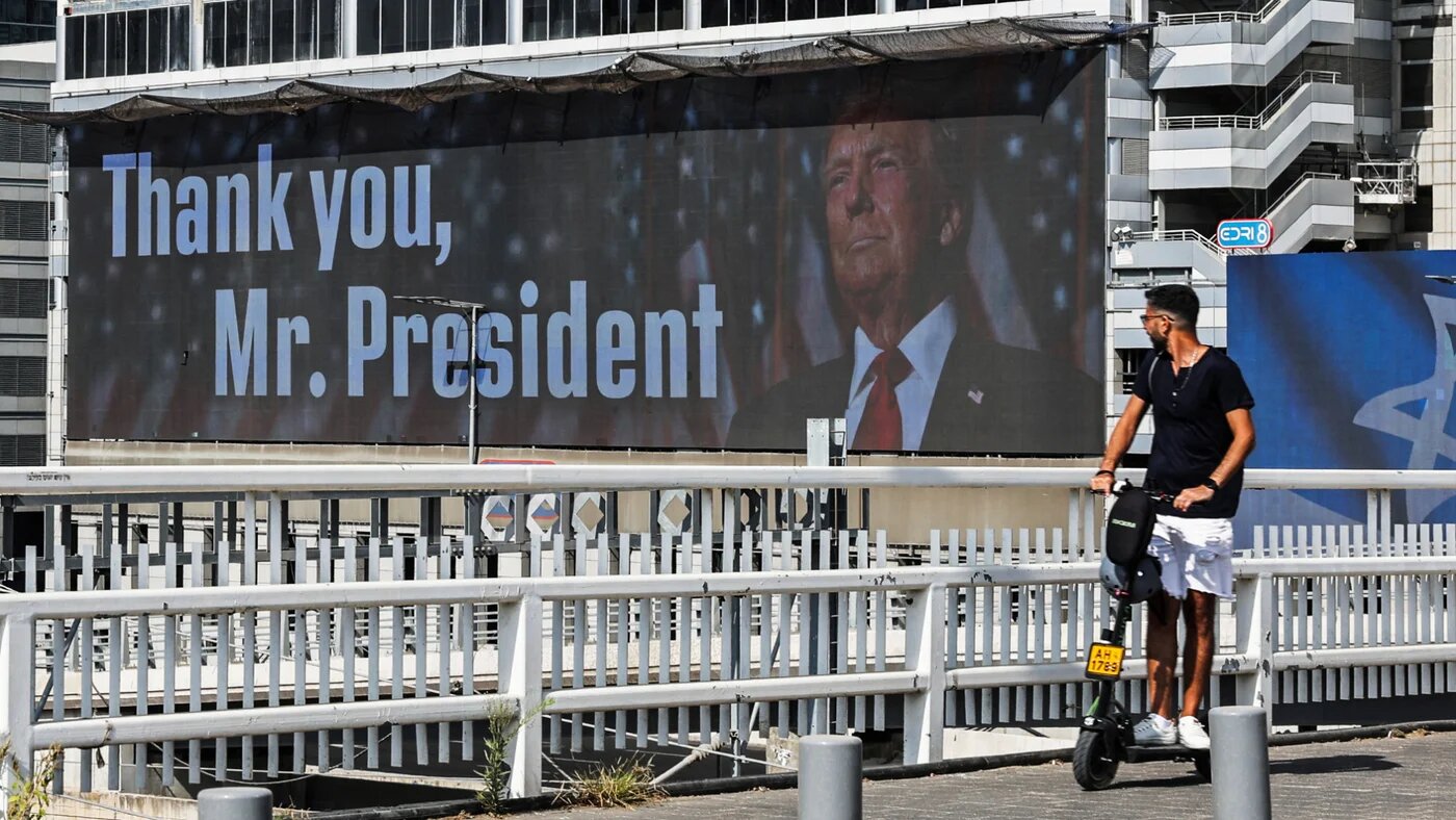 A man on an e-scooter passes a giant billboard, where US President Donald Trump appears, in Tel Aviv, Israel, 22 June 2025 (Reuters/Violeta Santos Moura)