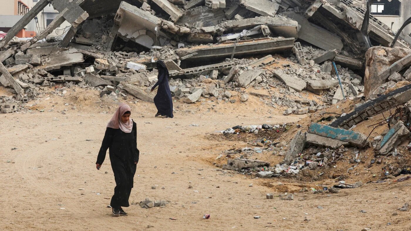 Palestinian women walk near rubble, after US President Donald Trump announced that Israel and Hamas agreed on the first phase of a Gaza ceasefire, in Khan Younis in the southern Gaza Strip 9 October 2025 (Reuters/Ramadan Abed)