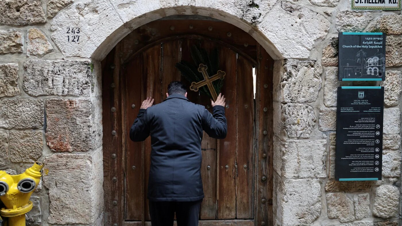 A Palestinian Christian holds a cross and a palm frond at the doors of the Church of the Holy Sepulchre after finding them locked in Jerusalem’s Old City, 29 March 2026 (Reuters/Ammar Awad)