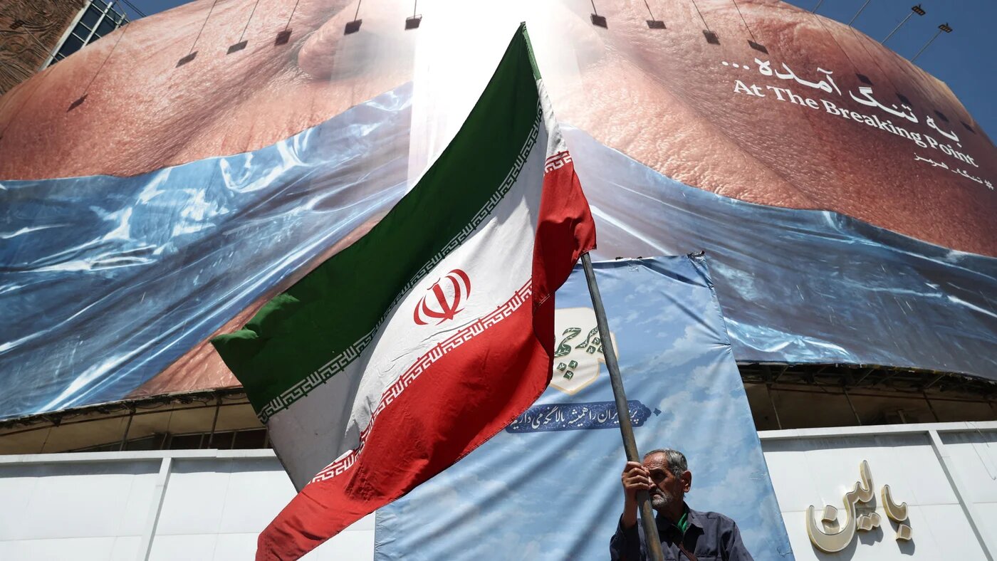 A man holds an Iranian flag near an anti-US billboard depicting US President Donald Trump and the Strait of Hormuz in Tehran on 30 May 2026 (Majid Asgaripour/WANA via Reuters)