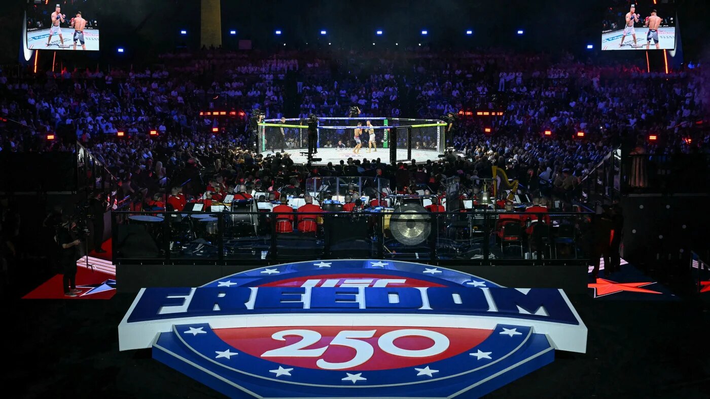 A large illuminated "Freedom 250" logo in red, white and blue stars-and-stripes design sits in front of a UFC fighting cage at the centre of a packed arena set up on the South Lawn of the White House, with large screens above showing two fighters
