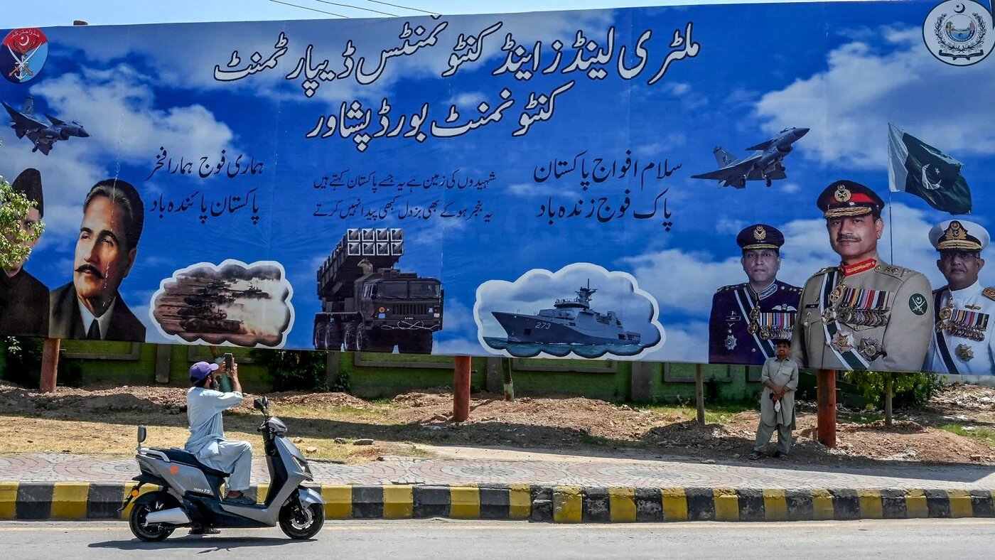 A man takes a picture of a billboard featuring Pakistan's Army Chief General Syed Asim Munir (C), Naval Chief Admiral Naveed Ashraf (R) and Air Chief Marshal Zaheer Ahmed Babar Sidhu in Peshawar, 15 May 2025 (Abdul Majeed/AFP)