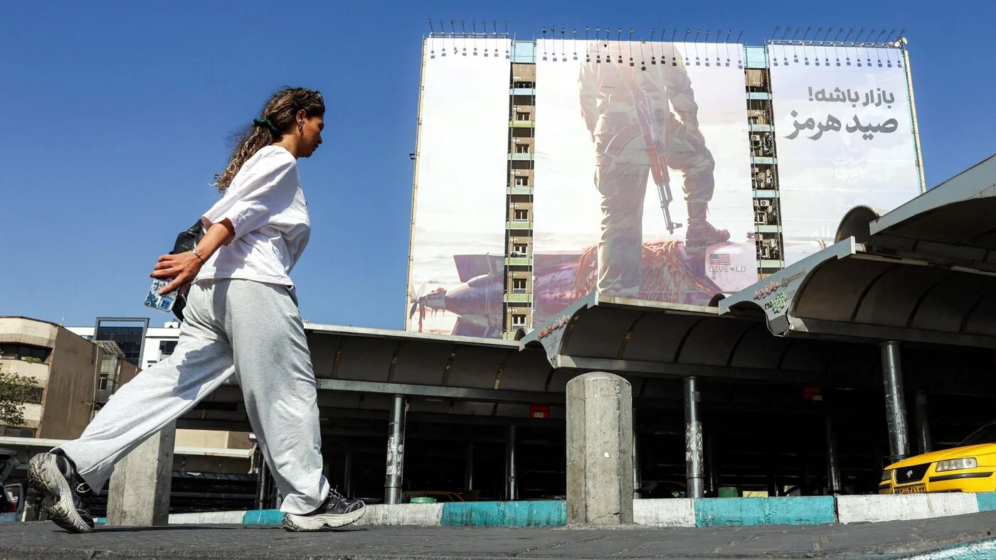 A woman walks past a billboard depicting an Iranian Revolutionary Guard placing his foot on a US sea drone reportedly seized by Iran, in Tehran, 24 September 2026 (AFP)