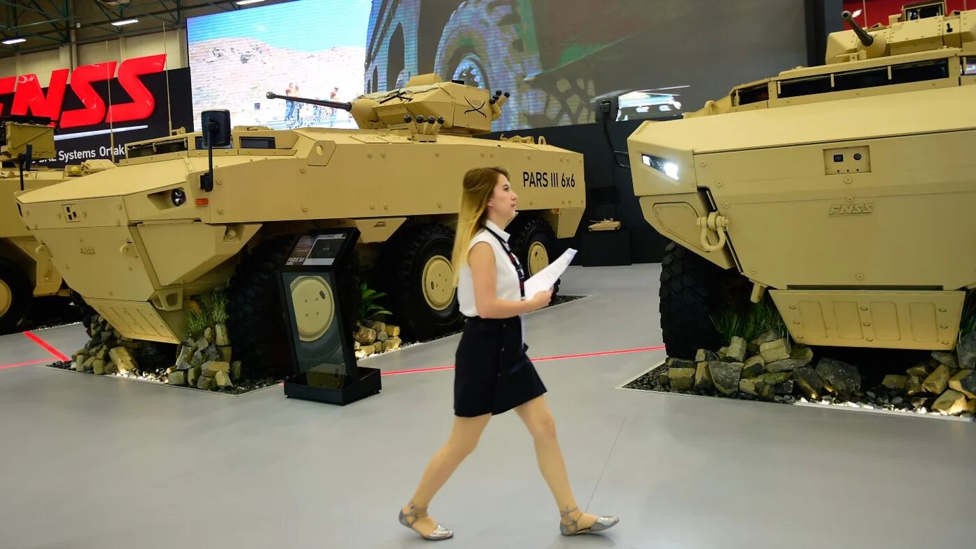 A woman walks past armoured vehicles at the International Defence Industry Fair in Istanbul, 9 May 2017 (Yasin Akgul/AFP)