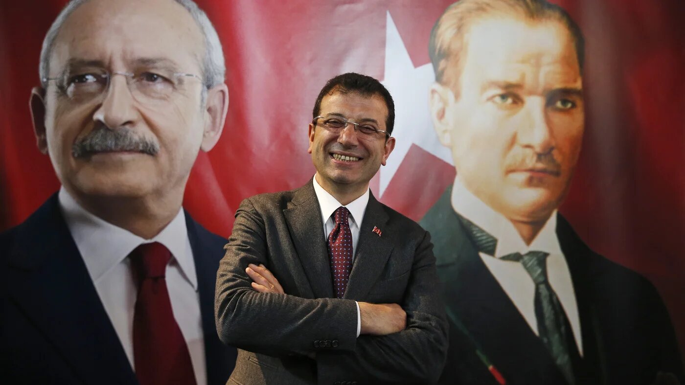 Backdropped by a poster of Kemal Kilicdaroglu, left, and Mustafa Kemal Ataturk, right, Ekrem Imamoglu poses for a photo in 2019 (AP)