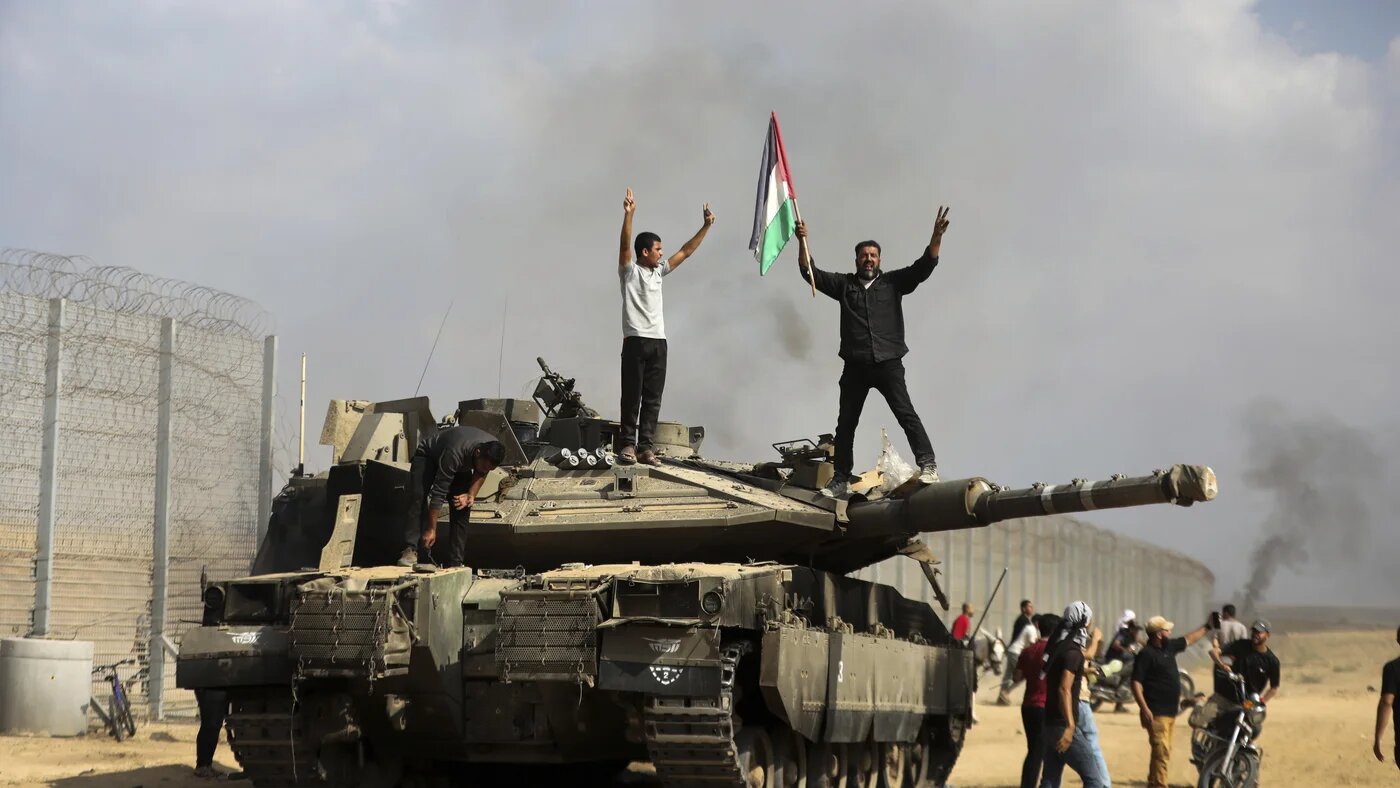 Des Palestiniens brandissent leur drapeau national et se réjouissent sur un tank israélien détruit à la barrière avec la bande de Gaza, à l’est de Khan Younès, le 7 octobre 2023 (AP)