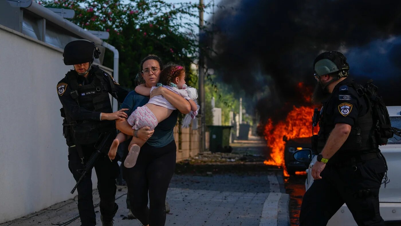Police officers evacuate a woman and a child from a site hit by a rocket fired from the Gaza Strip, in Ashkelon, 7 October (AP)