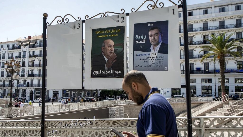 A man browses his phone as he walks past posters for presidential election candidates Abdelmadjid Tebboune (left) and the Socialist Forces Front's Youcef Aouchiche in Algiers, in September 2024 (AFP)
