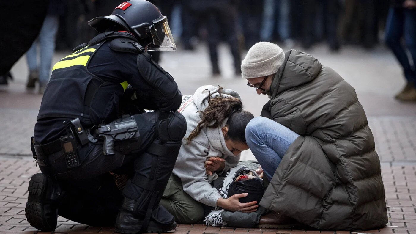 A police officer watches demonstrators helping a bloodied protester near Dam Square during a Pro-Palestine protest in Amsterdam on 10 November 2024 (AFP)