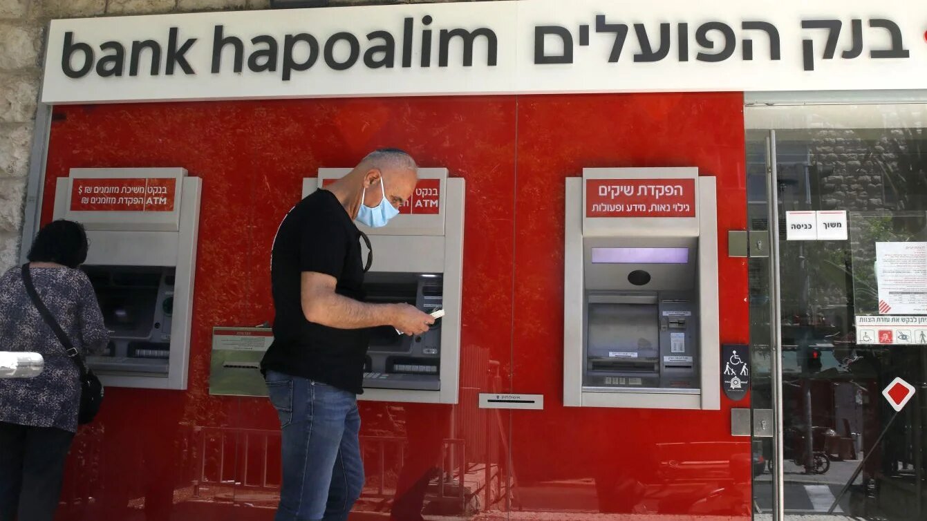 An Israeli man stands beside an automated teller machine at a Bank Hapoalim branch in Jerusalem, 1 May 2020 (Menahem Kahana/AFP)