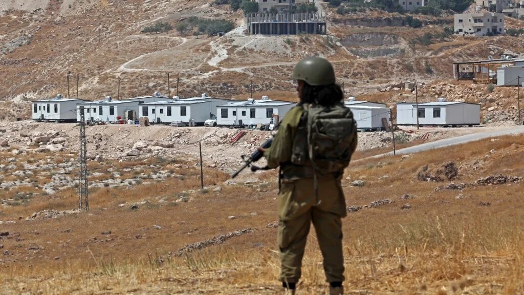 An Israeli soldier stands guard against the backdrop of newly established Israeli settlement outpost in Beit Sahur, south of Bethlehem, in the occupied West Bank on 14 August 2026 (AFP)