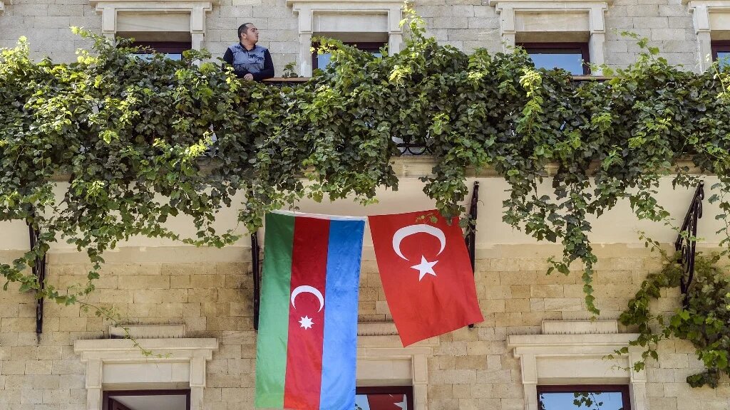A man stands on the balcony of a hotel with its facade decorated with flags of Azerbaijan and Turkey in the Old Town of Baku on 14 October 2020 (Tofik Babayev/AFP)