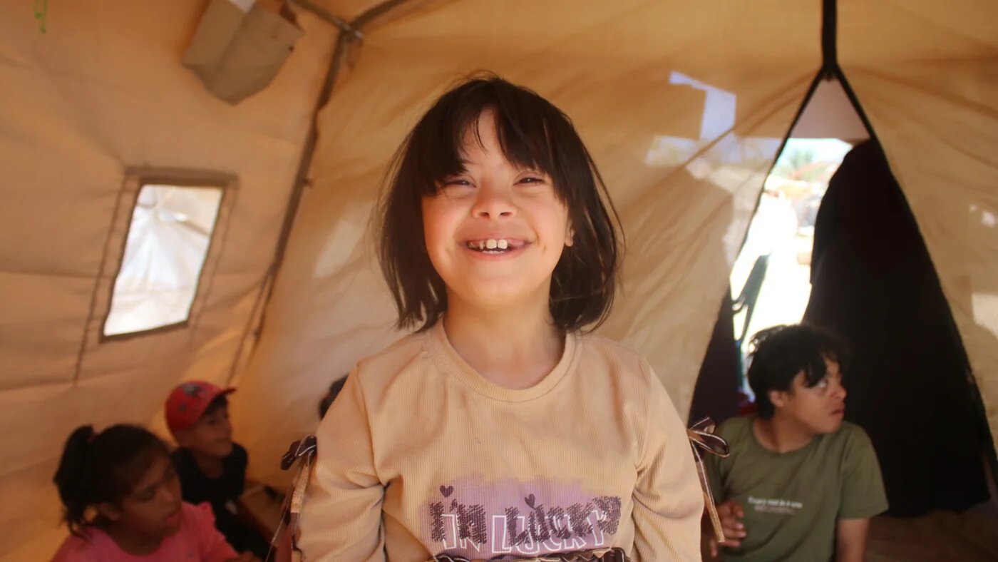 A child with Down syndrome smiles during a class held inside a makeshift tent in central Gaza (MEE/Abdallah al-Naami)