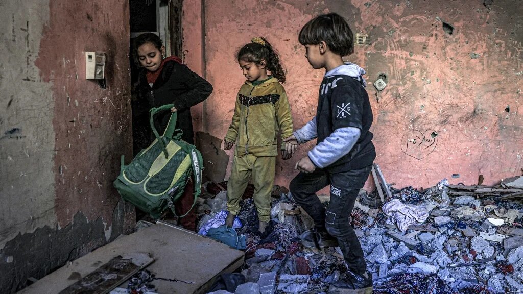 Children inspect items in the rubble in a room overlooking a building destroyed by Israeli bombardment in Rafah in the southern Gaza Strip on 24 December 2023 (Said Khatib/AFP)