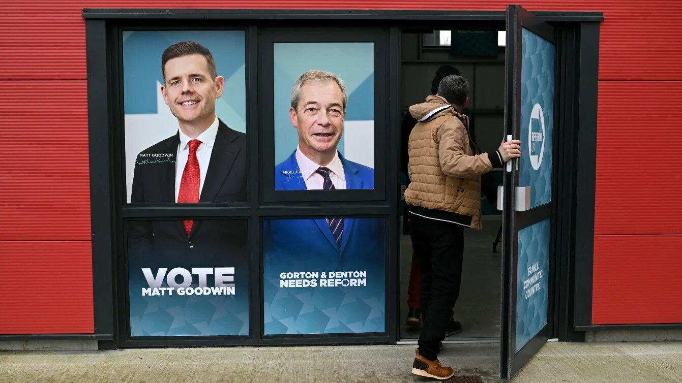 A person walks through a doorway printed with the faces of Reform UK candidate Matt Goodwin and Reform UK leader Nigel Farage in Denton, northwest England, on 5 February  2026. Oli SCARFF / AFP 
