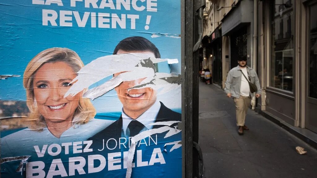 A man walks past an electoral poster of the National Rally (RN) with defaced portraits of party president Jordan Bardella (R) and leader of parliamentary group Marine Le Pen (L), in Paris on 10 June (Joel Saget/AFP)