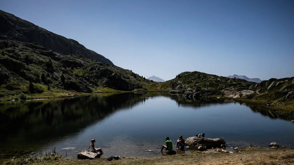 People sit beside a lake above L'Alpe d’Huez in the French Alps, 23 August 2023 (Jeff Pachoud/AFP)