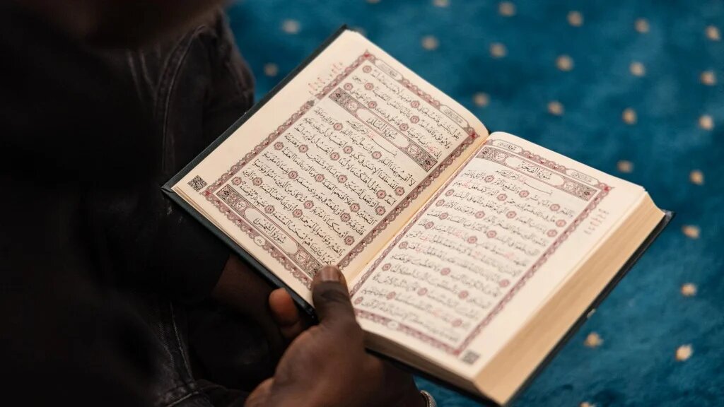 A man reads the Quran as Muslims wait to break their fast at a mosque during the month of Ramadan in Calais, northern France, on 10 March 2026 (Sameer al-Doumy/AFP)