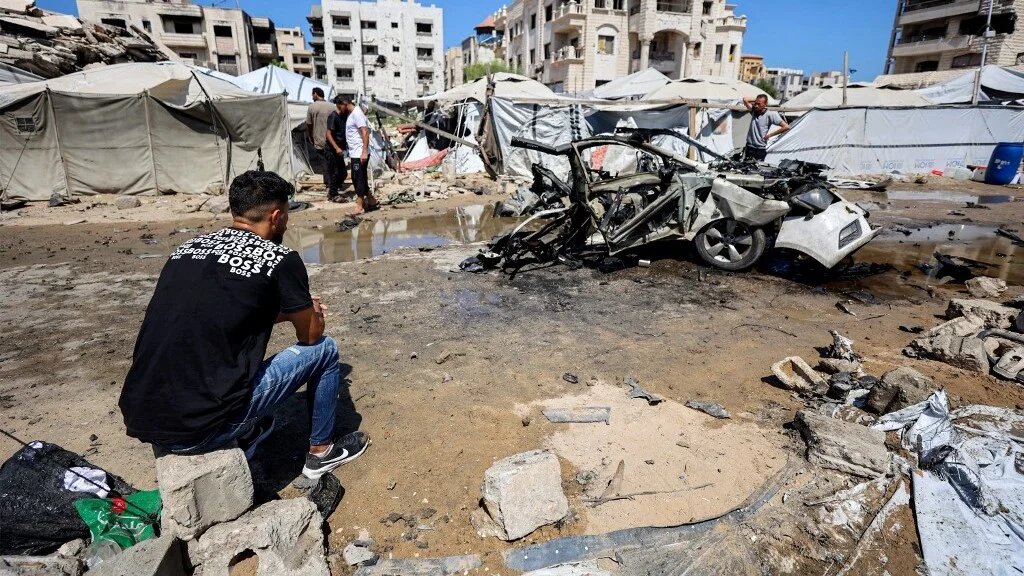 A man sits near a destroyed vehicle following an Israeli strike in the Rimal neighbourhood of Gaza City on 1 September 2026 (Omar al-Qattaa/AFP)