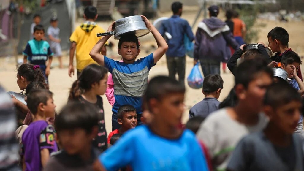Displaced Palestinian children line up to receive food in Rafah on 19 May 2024 (AFP)