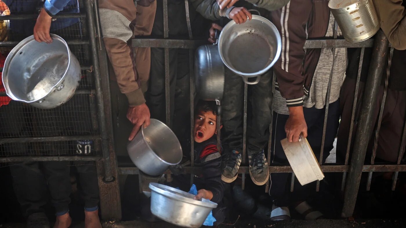 Palestinians gather to receive food being distributed along the roadside at the Nuseirat refugee camp in January (Eyad Baba/AFP)