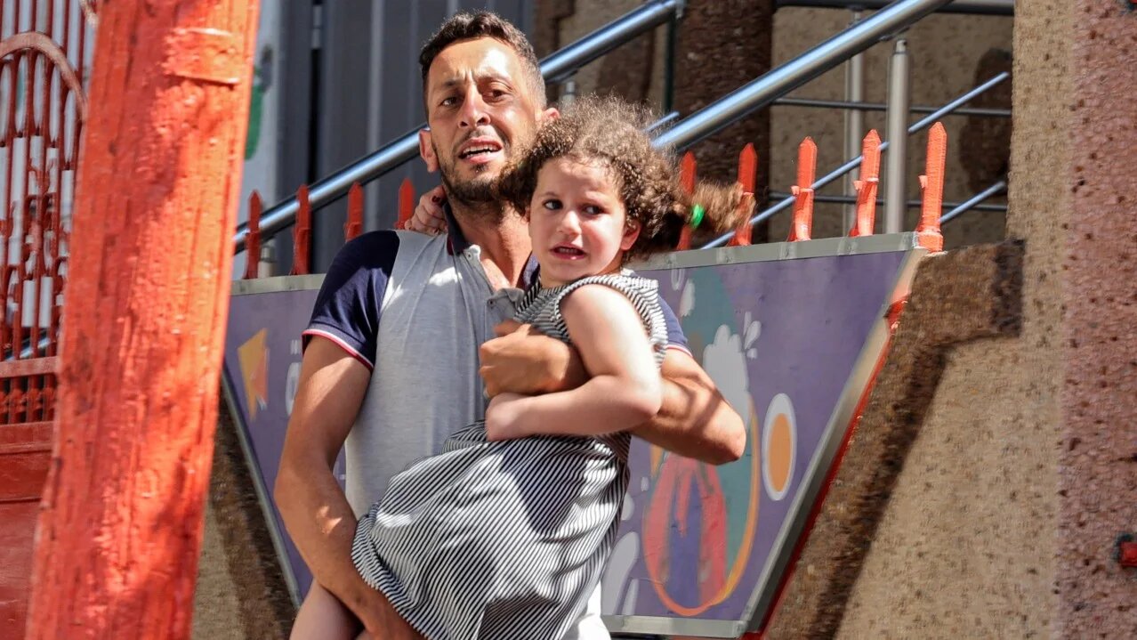 A Palestinian man carries his daughter after evacuating his home during an Israeli air strike in Gaza City, on 7 August, 2022 (AFP)