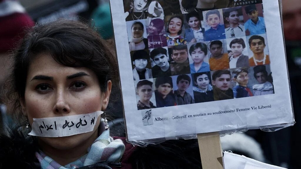 A demonstrator wears a sticker over her mouth with the words 'no execution' next to the portraits of alleged victims of crackdowns, during a silent march in Paris on 31 January 2026 (Sebastien Dupuy/AFP)